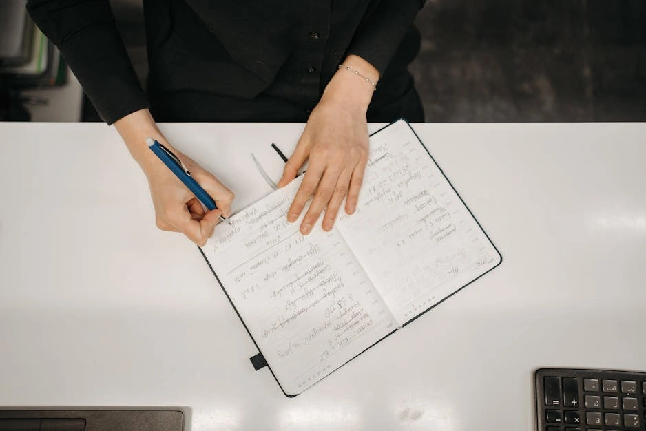 Osoba píšící si poznámky do zápisníku během studia.
